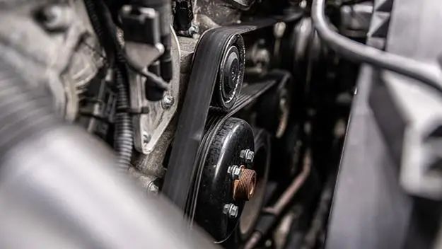 The Mufflerman, Mechanic Near Me Close-up of a car engine showing a serpentine belt in motion, with pulleys and other components visible. This image, perfect for Belts and Hoses Service references, highlights the intricate details of the engines mechanical parts.