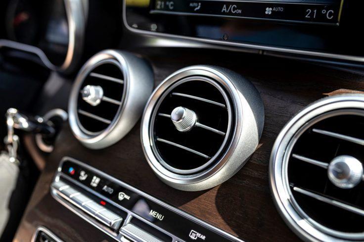 The Mufflerman, Mechanic Near Me Close-up of a cars dashboard featuring circular air vents with metallic trim on a woodgrain panel. Below the vents are buttons and controls, set against a sleek, modern design—perfect for learning 7 tips for keeping your cars air conditioning in top shape as sunlight casts subtle highlights.