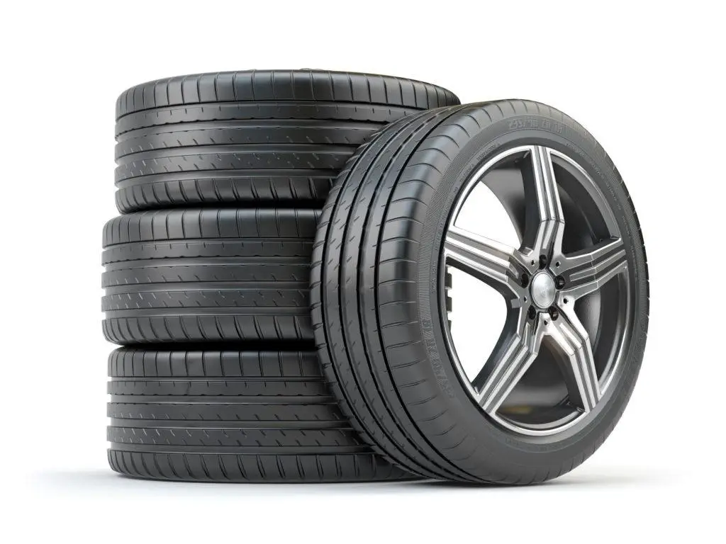 The Mufflerman, Mechanic Near Me A stack of four black tires with tread patterns is on the left, and an additional tire slightly leans against them on the right, ready for action at The Mufflerman. The tires are clean and placed on a pristine white background, highlighting their quality.