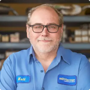 The Mufflerman, Mechanic Near Me A bearded man with glasses, labeled Matt from Muffleman Complete Auto Service, stands before shelves brimming with parts. Your go-to mechanic in East London, hes ready to assist anyone searching for auto repair in East London near me.