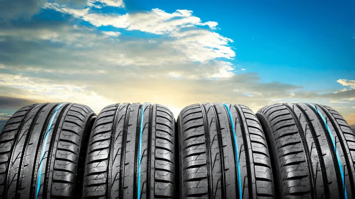 The Mufflerman, Mechanic Near Me Five car tires with blue stripes are aligned in front of a vibrant sky. The sun is setting, casting a warm glow, and clouds are scattered across the blue sky—a perfect backdrop to reflect on pothole damage repair needs in Southern Ontario.