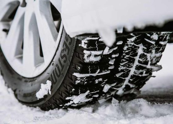 The Mufflerman Close-up of a car tire on a snowy surface, with snow clinging to its treads—an ideal scene for showcasing the Ontario Winter Tire Insurance Discount. The wheel is partially visible, and compacted snow emphasizes the need for reliable winter tires.