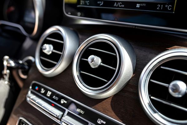 The Mufflerman, Mechanic Near Me Close-up of a cars dashboard featuring circular air vents with metallic trim on a woodgrain panel. Below the vents are buttons and controls, set against a sleek, modern design—perfect for learning 7 tips for keeping your cars air conditioning in top shape as sunlight casts subtle highlights.