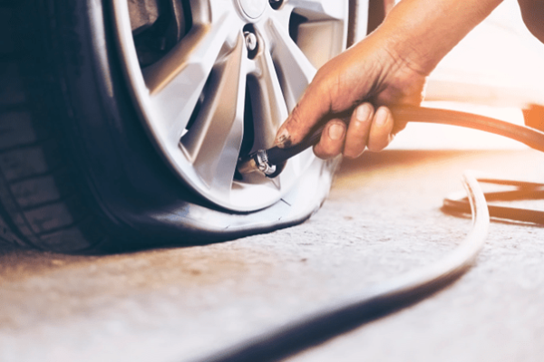 The Mufflerman, Mechanic Near Me A persons hand inflates a car tire with a black hose connected to the valve as sunlight gently illuminates the scene, casting soft shadows on the ground. The tire and rim are in focus, showing detail—just a glimpse of what youd expect at a Quick Tire Repair Centre.