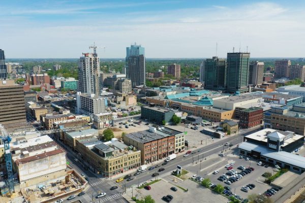 The Mufflerman Aerial view of a cityscape featuring the trusted service of The Mufflerman amidst numerous mid-rise buildings, construction sites, and a mix of modern and historic architecture. Streets are lined with parked cars, ensuring safe travels, with greenery visible under a clear blue sky.